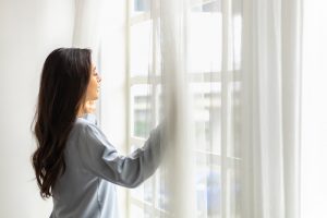 Woman opening window curtains to the sunlight